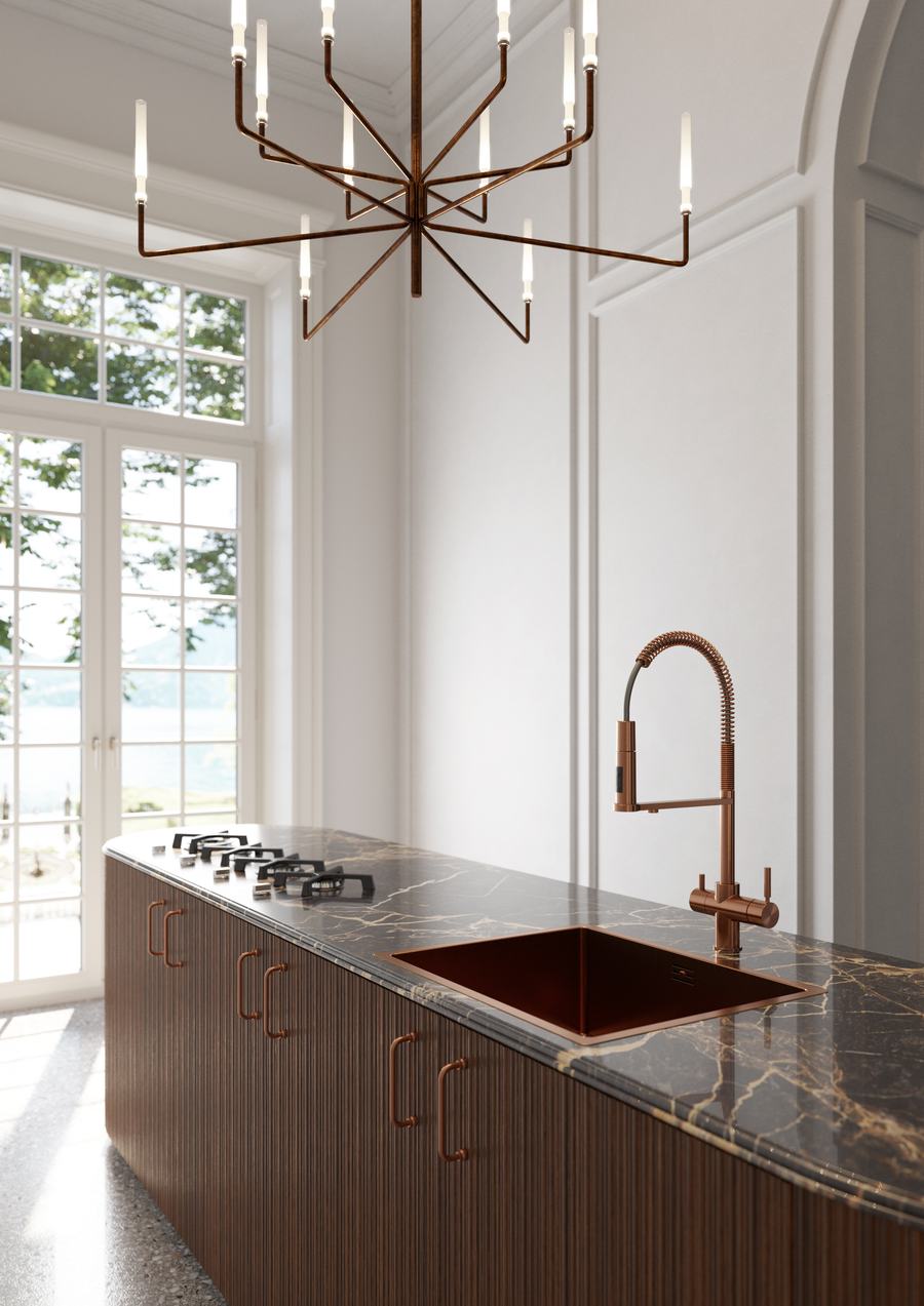 Cucina con piano in marmo scuro, rubinetto in rame e lampadario sospeso