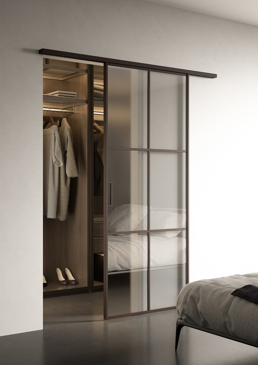 Cabina armadio con porta scorrevole in vetro e profili neri accanto al letto